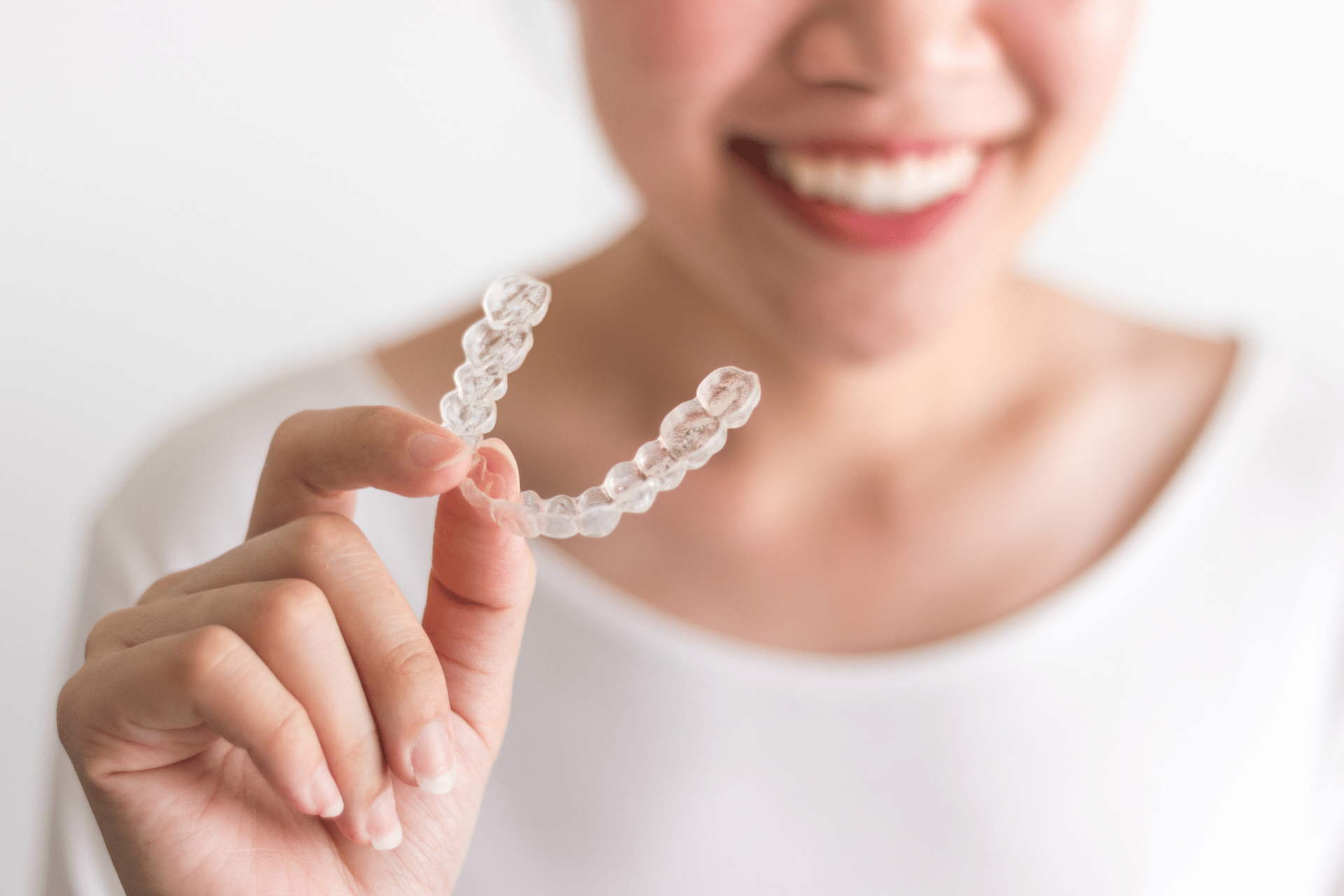 Smiling woman holding a clear Invisalign aligner near the camera