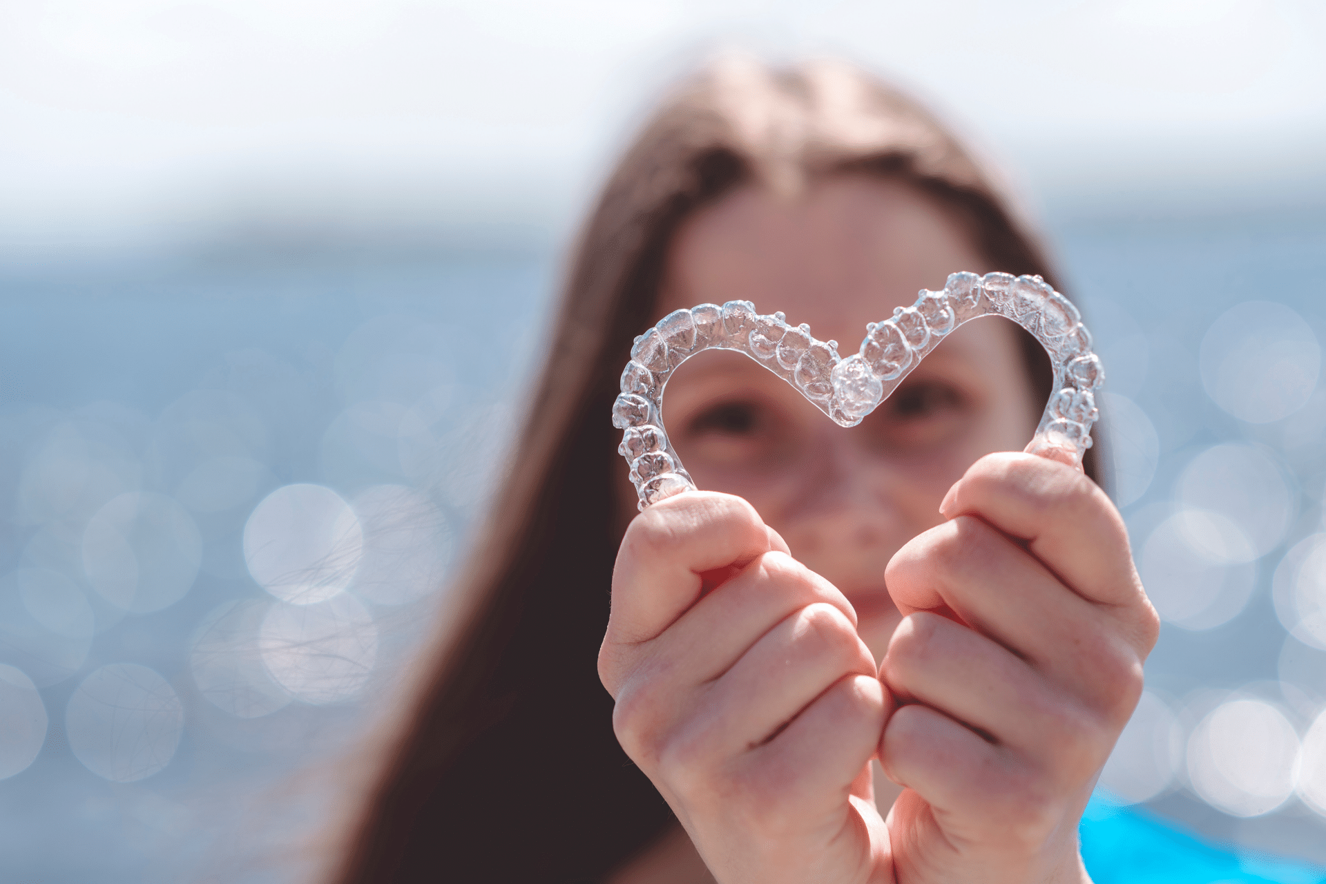 Woman holding two clear dental aligners together in the shape of a heart.